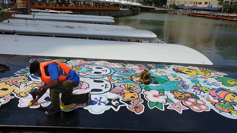 A worker in safety vest applying decal stickers on rooftop of a river cruise